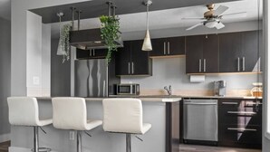 Una cocina moderna con armarios oscuros, una isla central con taburetes de bar, un microondas y un ventilador de techo.