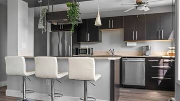 A modern kitchen with dark cabinets, a central island with bar stools, a microwave, and a ceiling fan.
