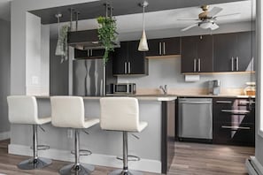 Cozinha moderna com armários escuros, uma ilha central com banquetas, micro-ondas e ventilador de teto.
