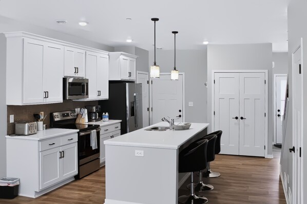 A modern kitchen with white cabinetry, stainless steel appliances, and a central island with bar stools.