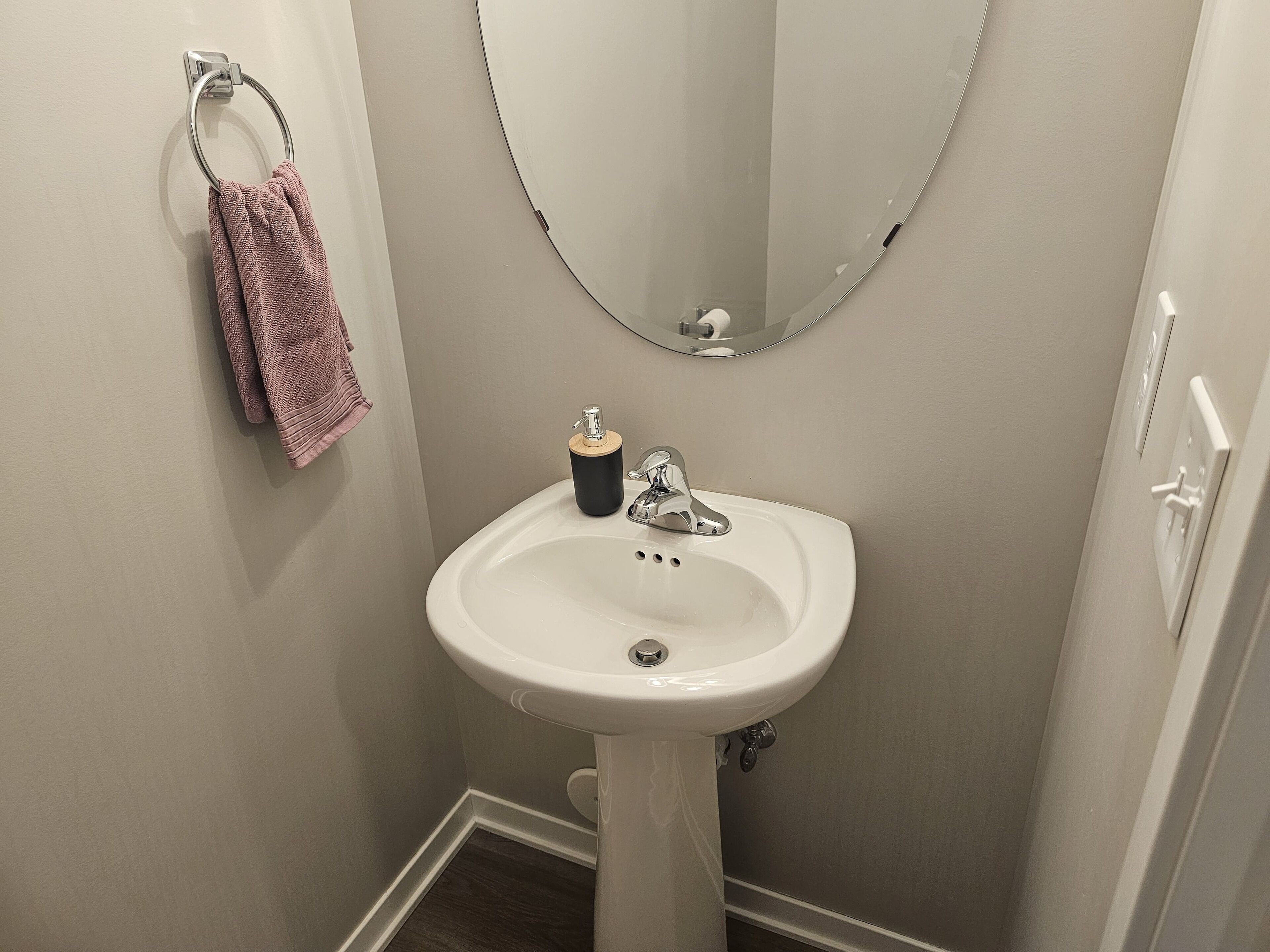 A bathroom with a white sink, a mirror, and a towel rack with a pink towel.