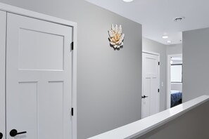A hallway with white doors, a decorative wall piece, and a staircase leading to another room.