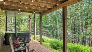 A wooden deck with a bench and a hot tub, surrounded by lush greenery.