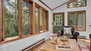 A cozy living room with large windows, a fireplace, a comfortable sofa, and a coffee table with books.