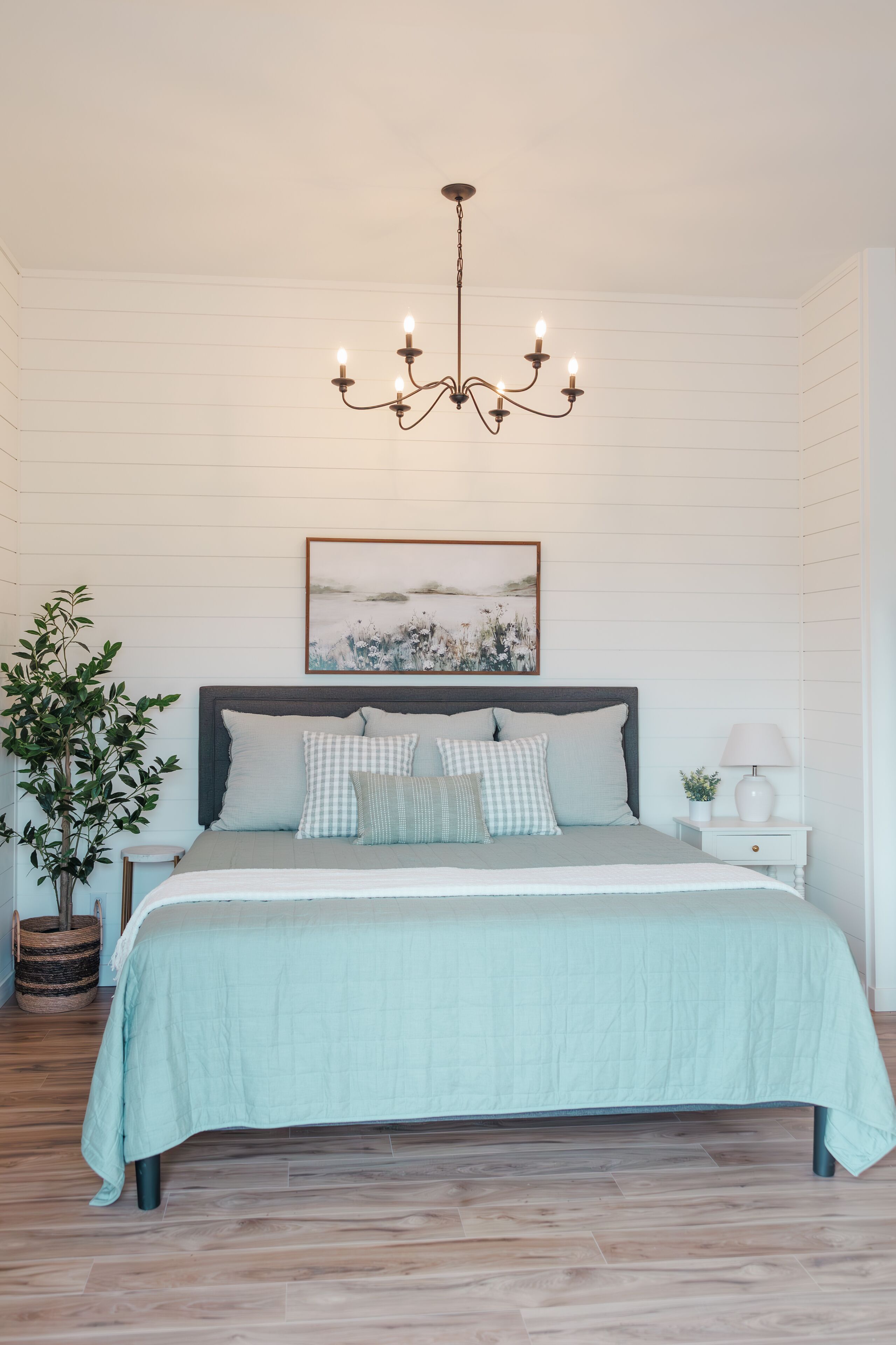 Ein Schlafzimmer mit einem Bett, einer Chandelüster, einem gerahmten Bild an der Wand und einem Blumentopf.