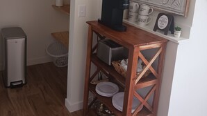 A compact kitchen with a coffee machine, a toaster, and a small shelf with plates and a coffee mug.