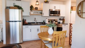 A modern kitchen with white cabinets, stainless steel appliances, and a wooden dining table with chairs.