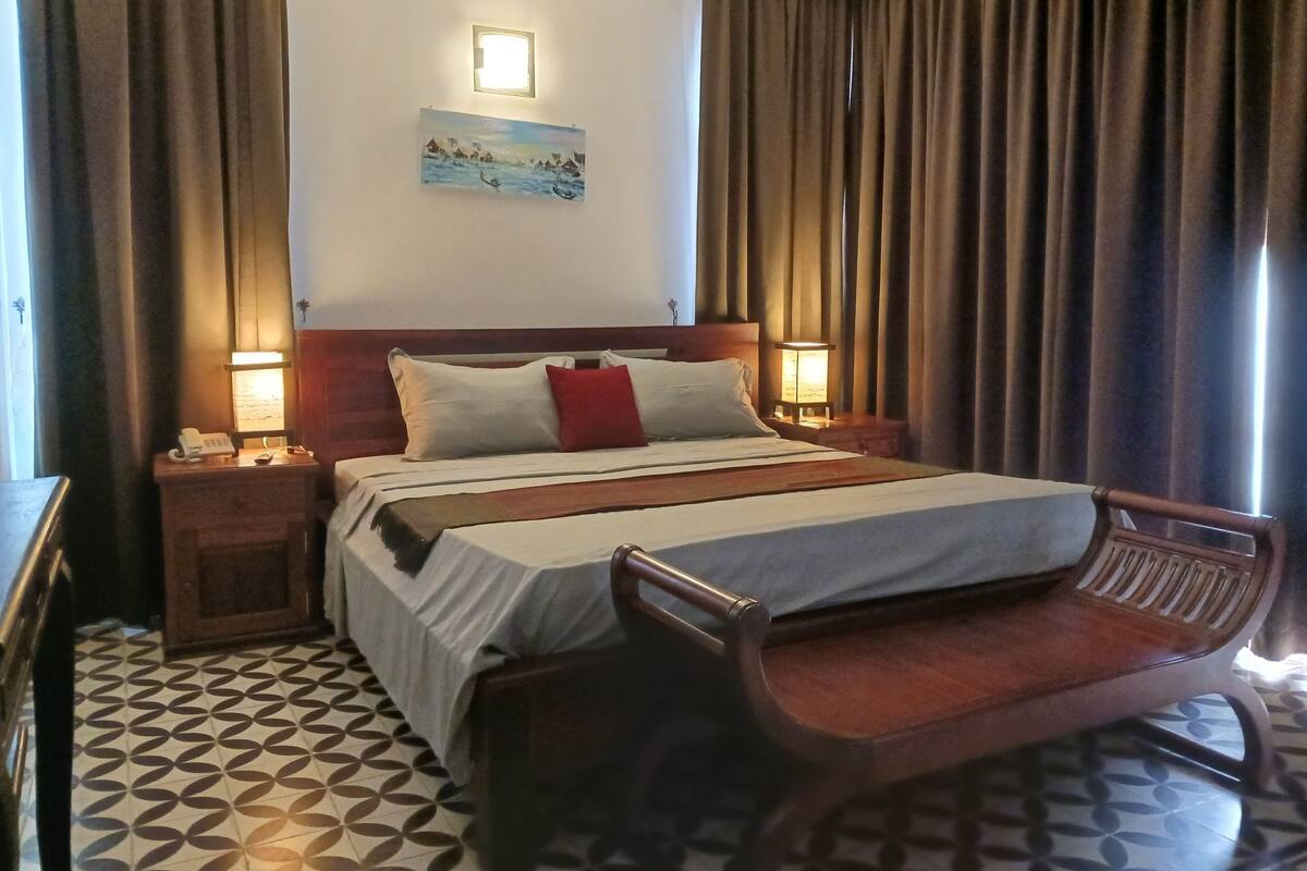 Une chambre d’hôtel avec un lit, deux lampes de chevet, un tableau au mur et une chaise en bois.