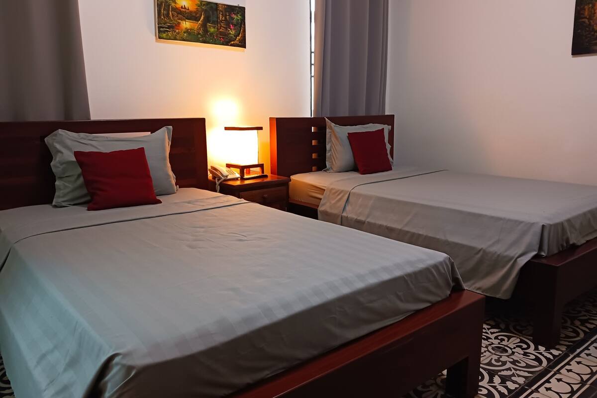 Une chambre d’hôtel avec deux lits simples, une table de chevet avec une lampe, un tableau au mur et un sol à motifs.