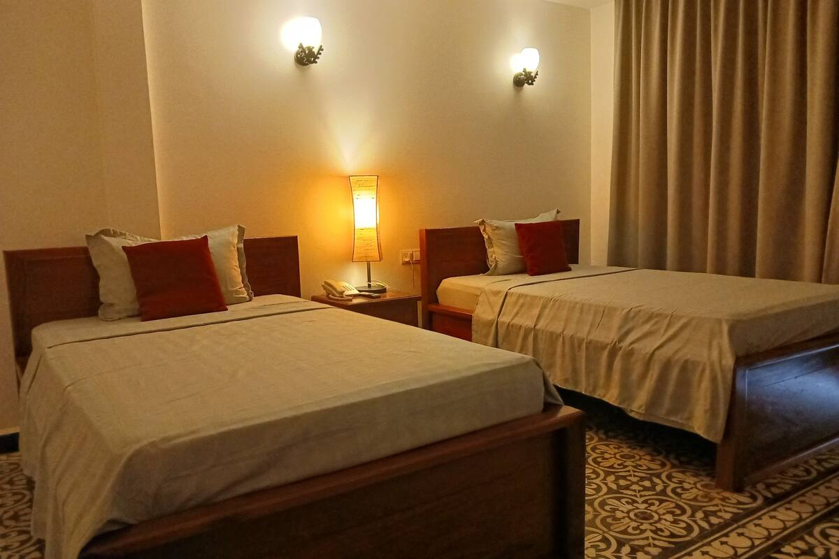 Une chambre d’hôtel avec deux lits, une table de chevet avec une lampe et une moquette à motifs.