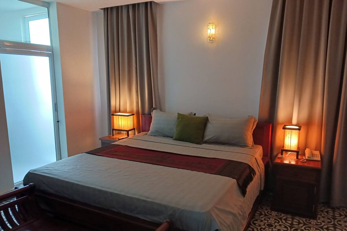 Une chambre d’hôtel avec un lit, deux tables de chevet avec des lampes, une chaise et un sol à motifs.