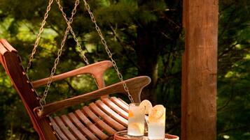 A wooden swing chair suspended by chains, a small table with two glasses of a clear beverage, and a wooden bench.