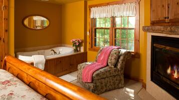 A bedroom with a wooden bed, a bathroom with a bathtub, a fireplace, and a window with a view of trees.