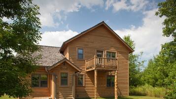 A wooden log cabin with a balcony, a front porch, and a small attached structure.