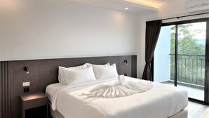 A modern hotel room with a large bed, a bedside table, a nightstand, and a window with a view of greenery. - GEEN Hotel Chonburi (Chonburi)