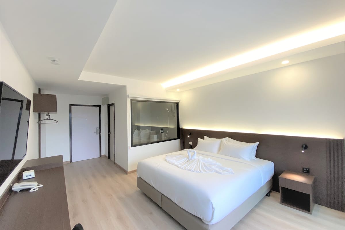 A modern hotel room with a large bed, a bedside table, a mirror, and a wardrobe.