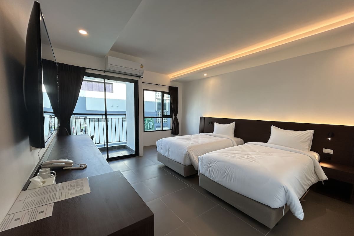 A hotel room with two beds, a TV, a desk with a computer, and a balcony with a view.