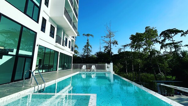 A modern building with a swimming pool, large windows, and a clear blue sky. - GEEN Hotel Chonburi (Chonburi)