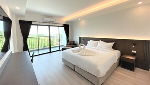 A hotel room with a large bed, a desk with a telephone, and a view of a balcony with greenery. - GEEN Hotel Chonburi (Chonburi)