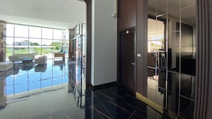 A modern hotel lobby with a glass door leading to a pool area, a reception desk, and a view of the outdoors. - GEEN Hotel Chonburi (Chonburi)
