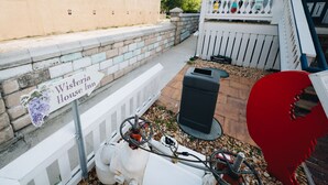 Ein Patio mit einem Schild, das "Wisteria House Inn" zeigt, einem weißen Zaun, einer schwarzen Mülltonne und einem roten dekorativen Gegenstand.
