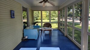 A covered porch with a ceiling fan, a blue sofa, a wooden table, and a chair. - 1910 Family Home near Lake Winnebago, available for EAA (Oshkosh)