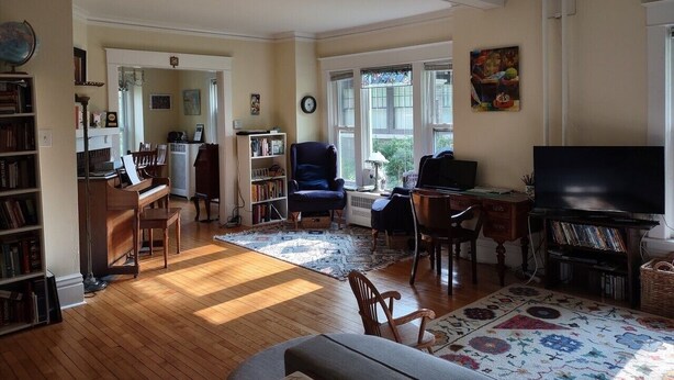 A spacious living room with a piano, a television, and a bookshelf. - 1910 Family Home near Lake Winnebago, available for EAA (Oshkosh)