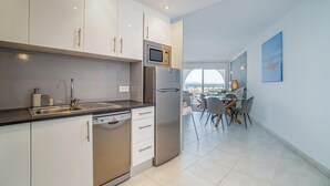 Een moderne keuken met witte kasten, roestvrijstalen apparatuur en uitzicht op een eethoek met een tafel en stoelen.