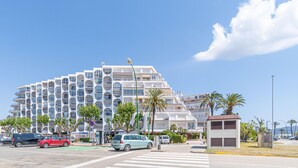 Een modern meerlaags hotel met balkons, een parkeerplaats en palmbomen.