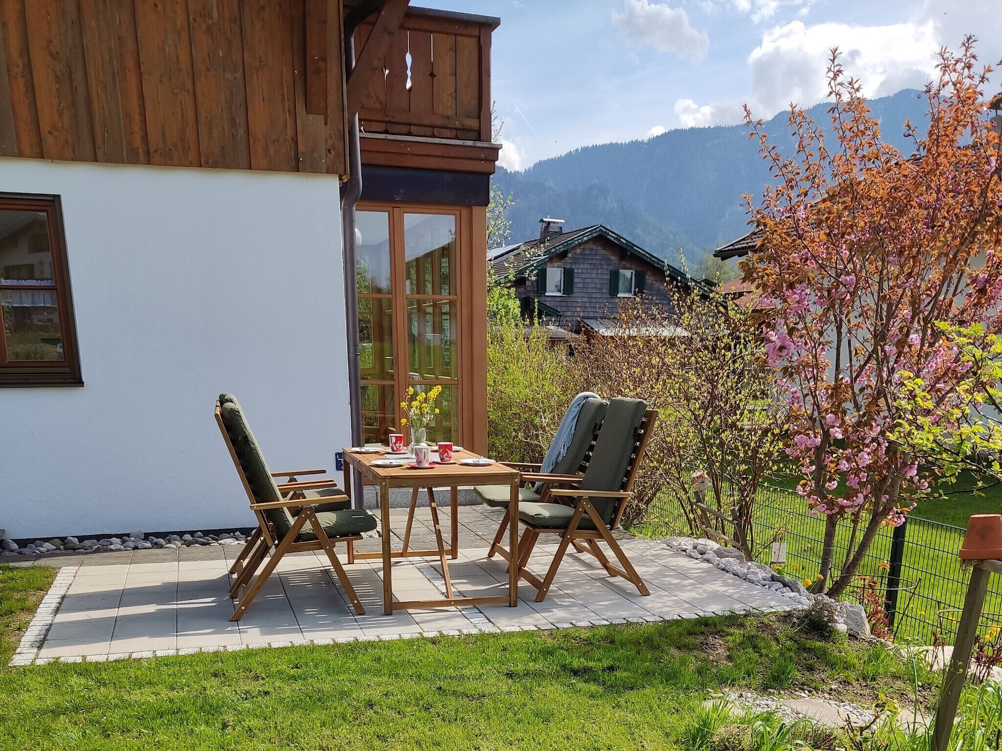 A patio with a table and chairs, a wooden deck, and a view of a mountain range.