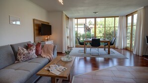 Una sala moderna con sofá, mesa de centro y comedor, con vista a áreas verdes.