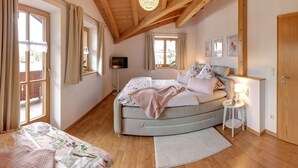 Un dormitorio con cama curva, vigas de madera en el techo, un candelabro y ventanas amplias.