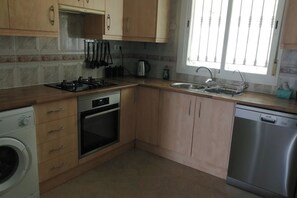 A kitchen with wooden cabinets, a stove, oven, washing machine, sink, and dishwasher.