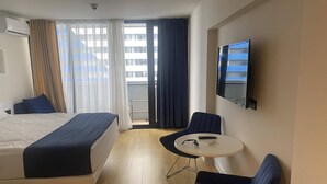 Habitación de hotel con cama, una mesita, dos sillas, televisión y balcón con cortinas.