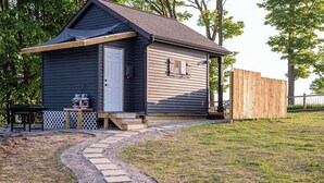 Un petit bâtiment d’un seul étage, doté d’un porche, d’une porte et d’une petite table avec un barbecue à l’extérieur.