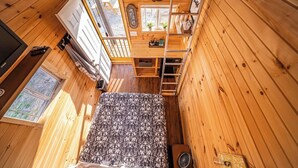 Une petite cabane en bois comprenant un lit, une petite cuisine et une fenêtre.