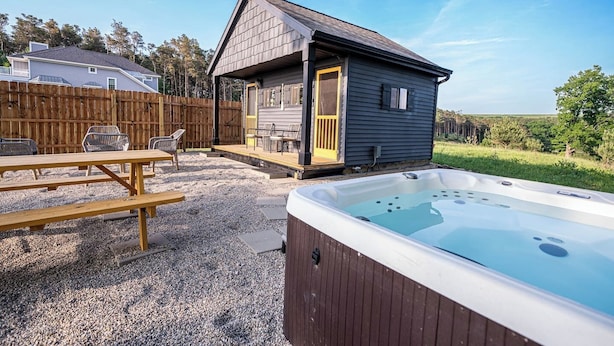 Une petite cabane avec un jacuzzi, une terrasse et une table de pique-nique, située dans un jardin.