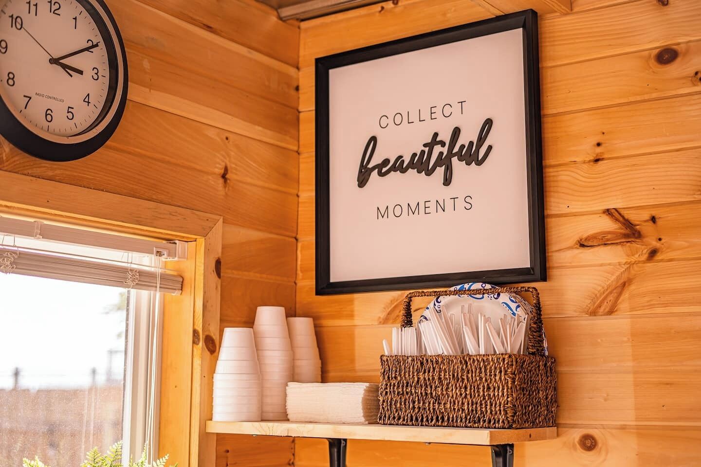 Un intérieur en bois avec une horloge, une citation inspirante encadrée, des tasses empilées et un panier.