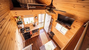 Une cabane avec une chambre à coucher située en mezzanine, un coin repas, une cuisine et un téléviseur.