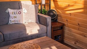 Une pièce chaleureuse avec un canapé gris, une petite table en bois, un ventilateur et une étagère avec des plantes.