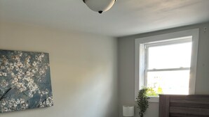 Makuuhuone, jossa on sänky, yöpöytä, lamppu, ikkuna ja seinälle ripustettu taideteos.