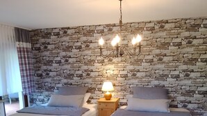 Un dormitorio con dos camas, una pared de piedra, una araña y una mesita de noche con lámpara.