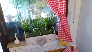 Una habitación con un banco de madera, un radiador blanco, un arreglo de plantas en macetas y un mantel a cuadros.