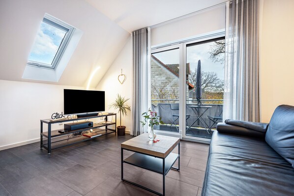 Een moderne woonkamer met een flatscreen televisie, een salontafel, een bank, een potplant en een glazen schuifdeur naar een buitenruimte.