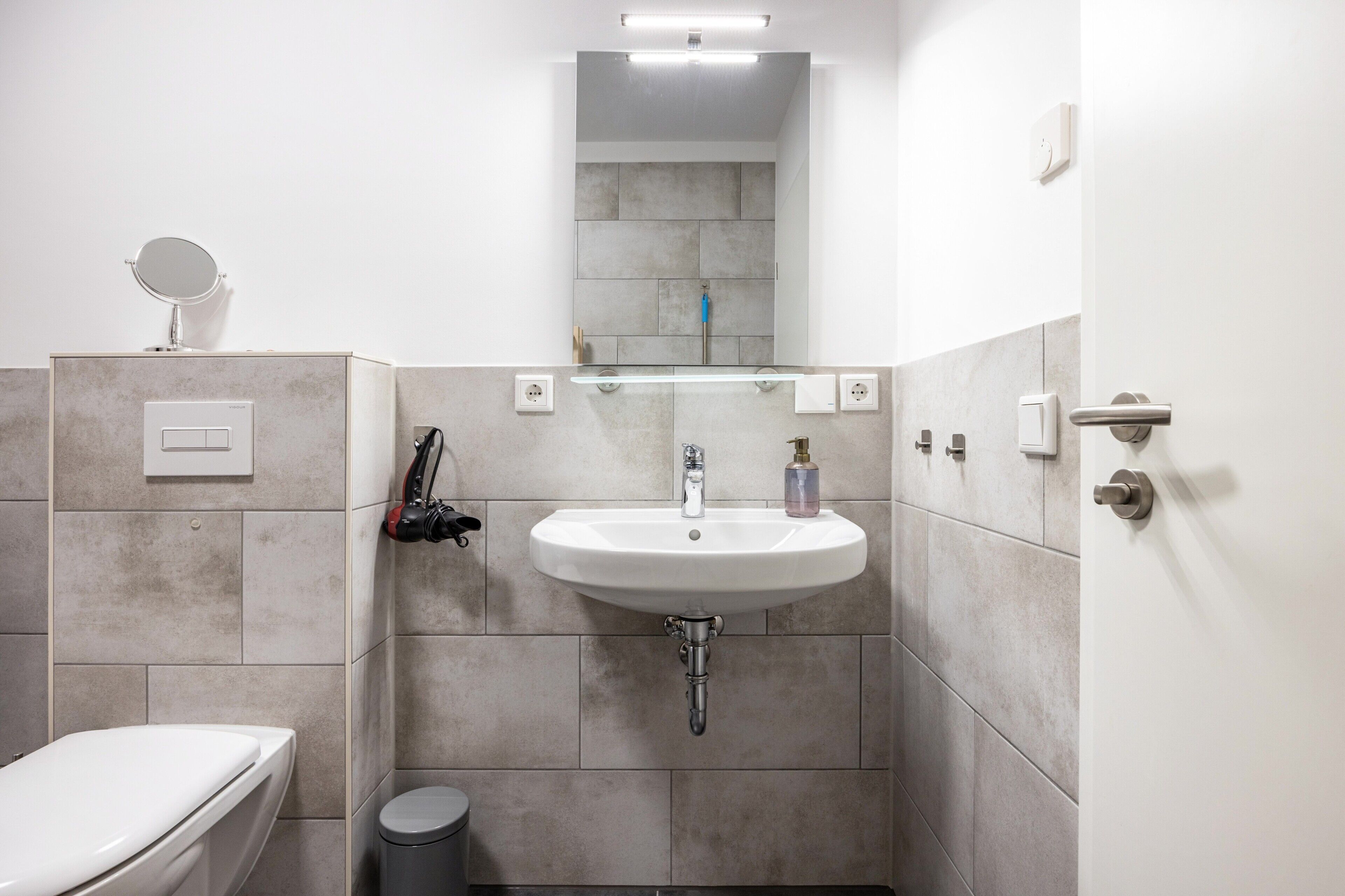 Un baño con lavamanos, espejo y retrete blancos.