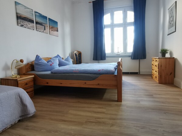 A bedroom with a wooden bed, a nightstand, a dresser, a window with curtains, and wall art.