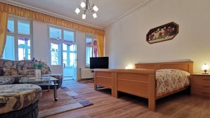 A room with a sofa, a bed, a television, a lamp, and a floral painting on the wall. - Apartment "Villa Adler - Seeblick" with Lake View (Seebad Ahlbeck)
