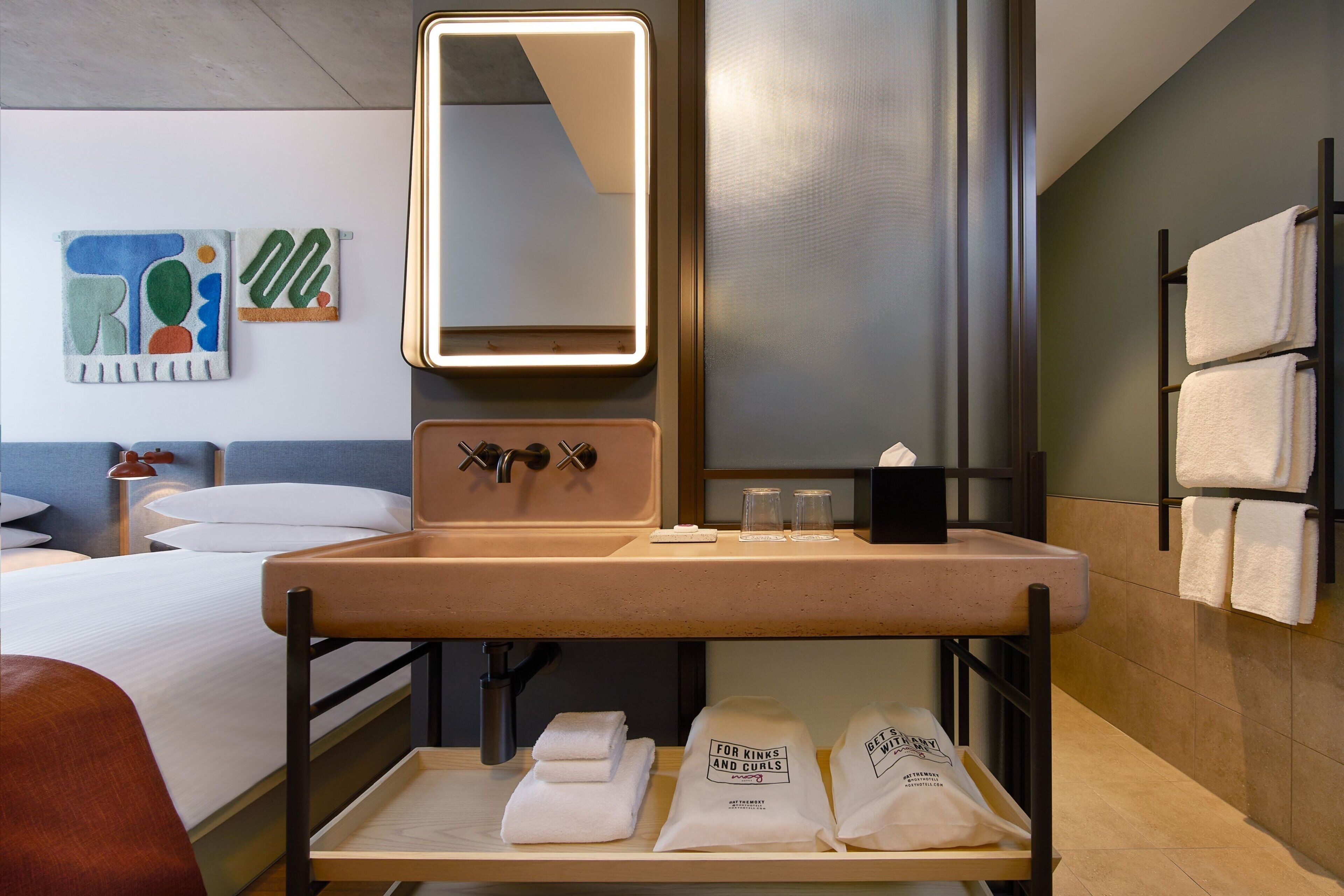 Habitació d'hotel amb un llit, una taula de nit, un mirall, un vàter i un escurapobrins.