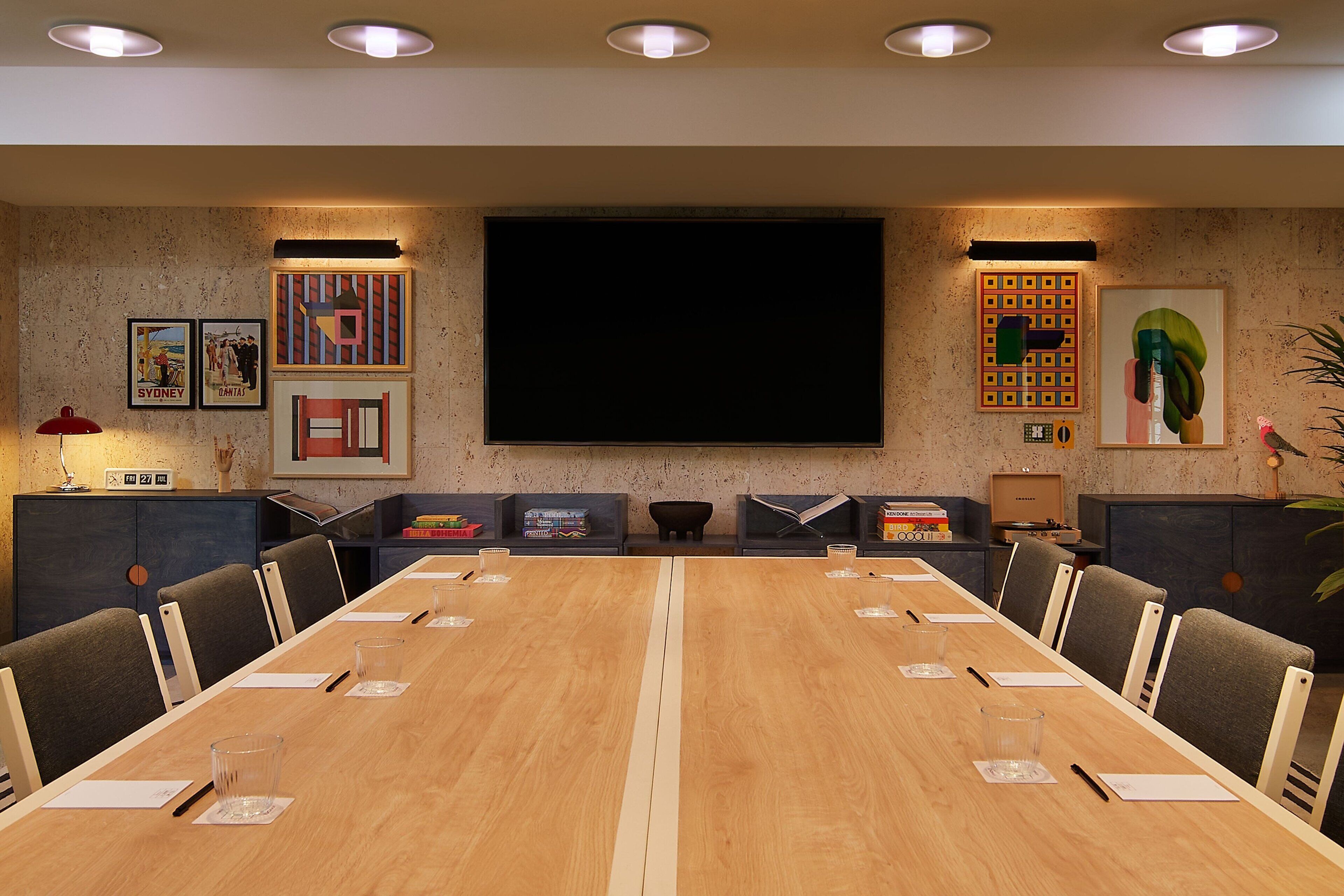 A conference room with a long table, chairs, a projector screen, and framed artwork on the walls.