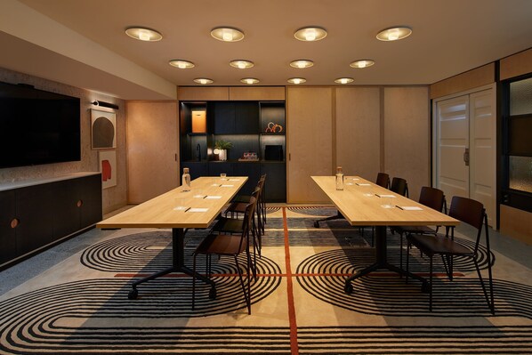 A conference room with a long table, chairs, a TV, and a patterned carpet. - Moxy Sydney Airport (Mascot)